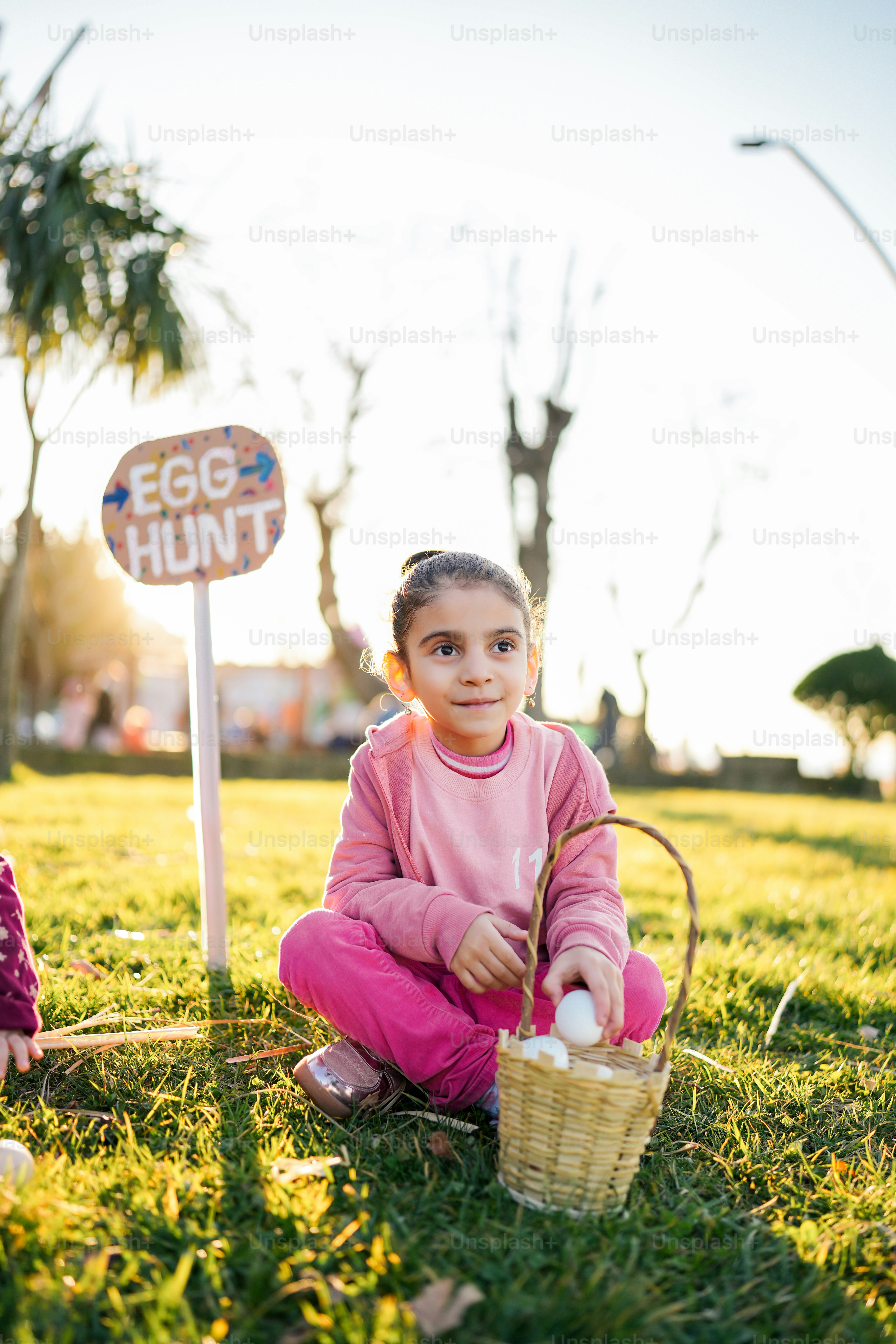 a little girl sitting in the grass with a basket of eggs