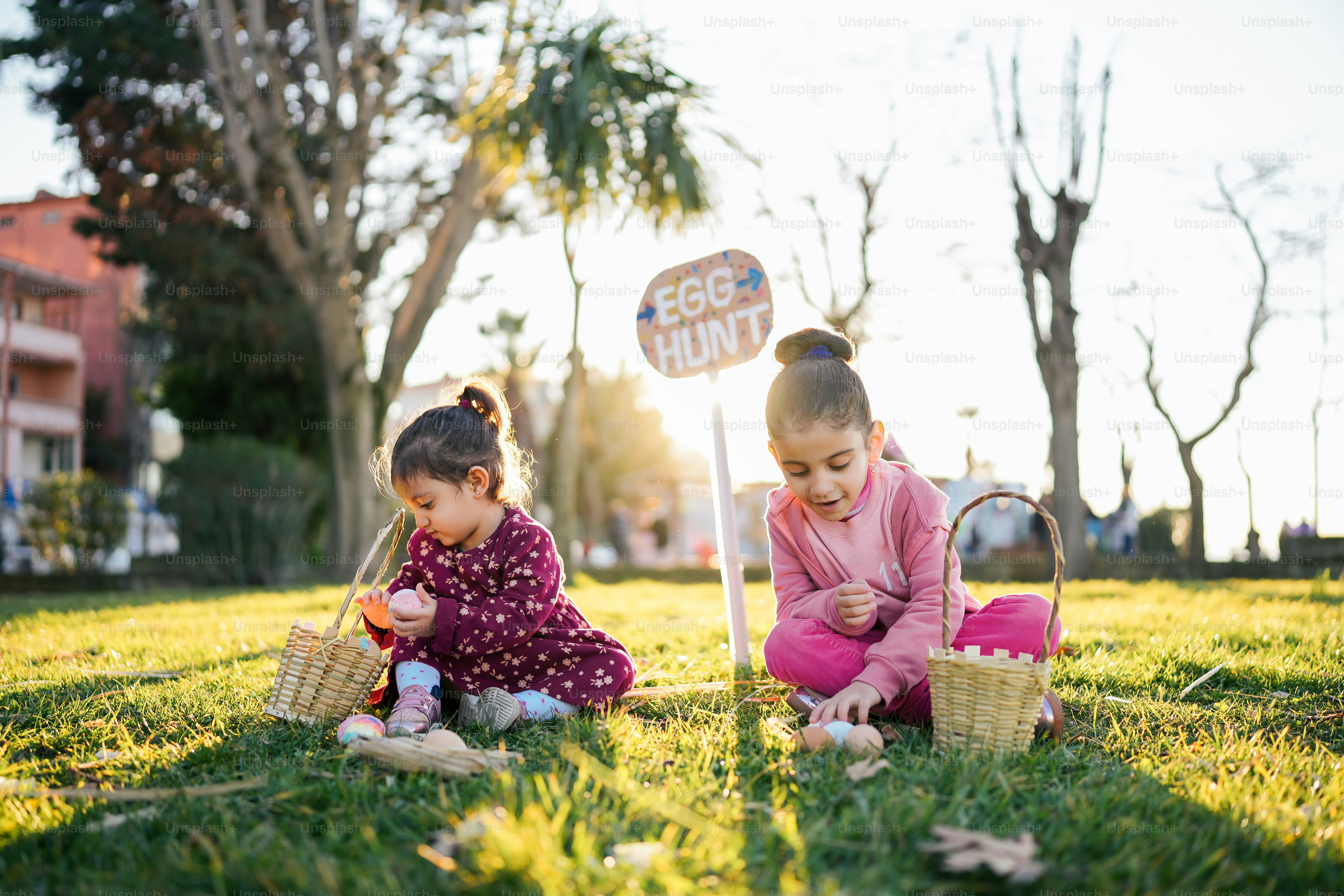 two little girls sitting in the grass playing with a basket
