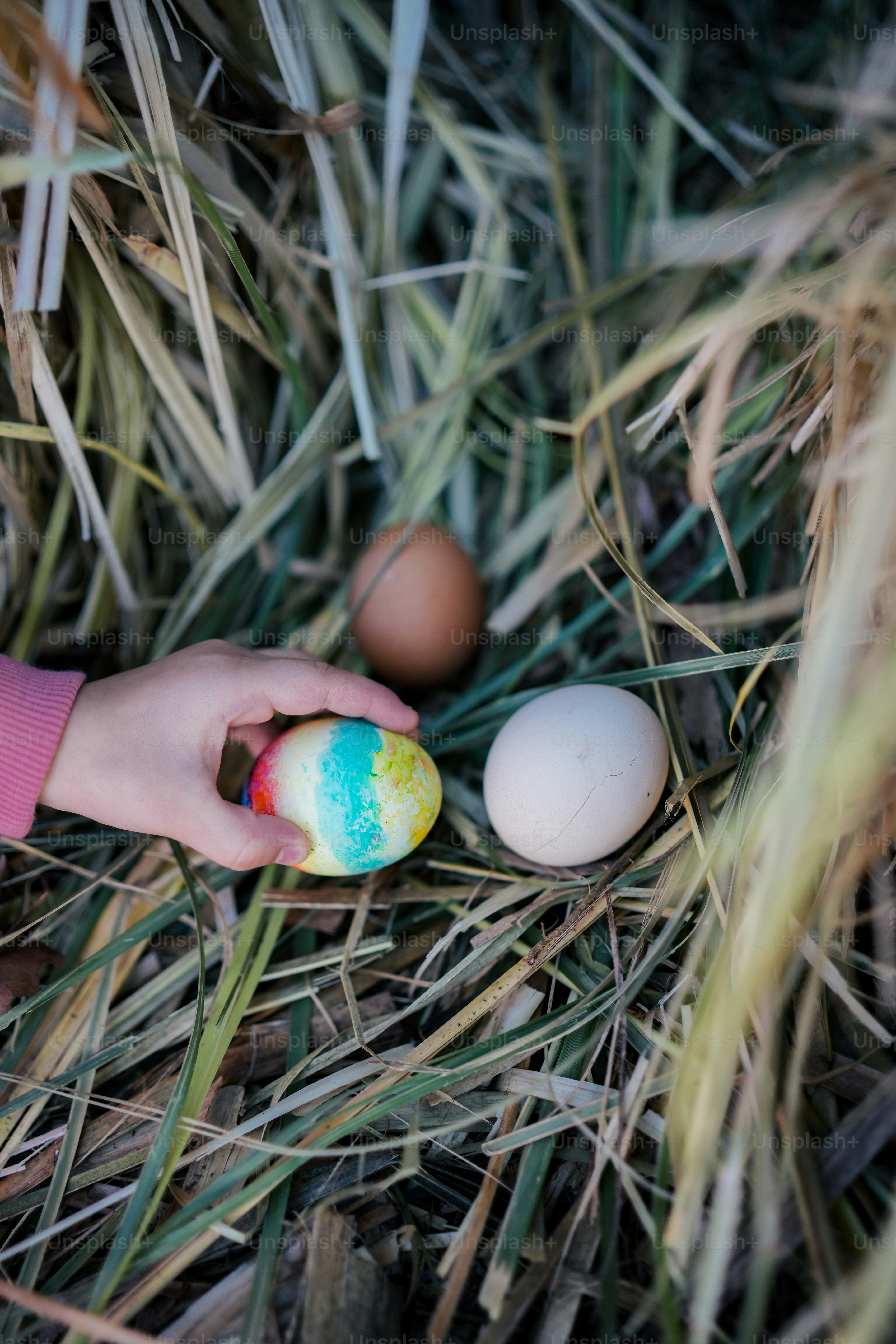 a child's hand holding a painted egg in the grass