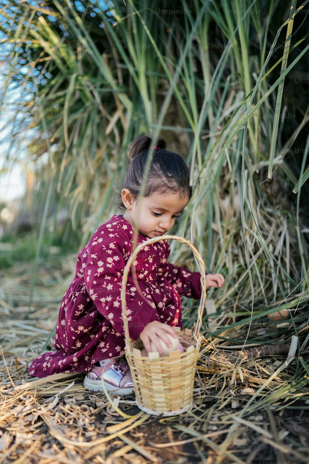 a little girl sitting on the ground with a basket