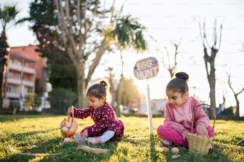 two little girls sitting in the grass playing with a basket