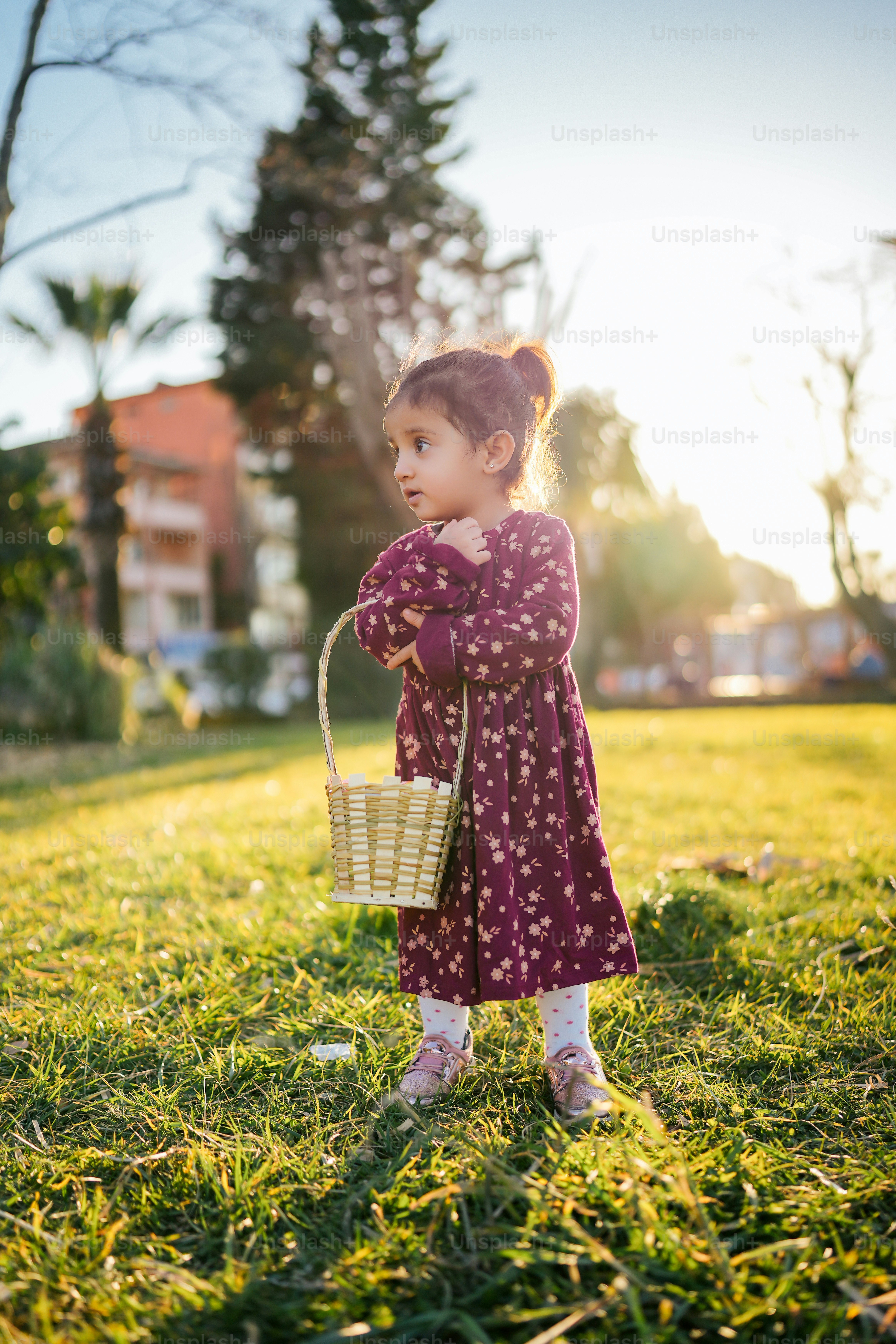 Seorang gadis kecil berdiri di rumput sambil memegang keranjang