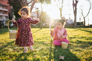 two little girls sitting in the grass with baskets of eggs