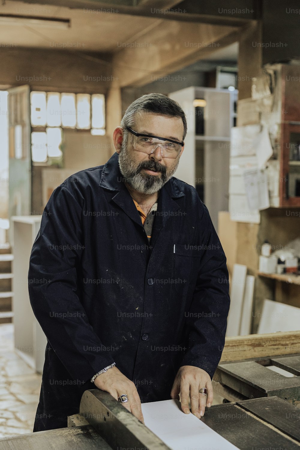 a man with a beard and glasses standing next to a piece of wood