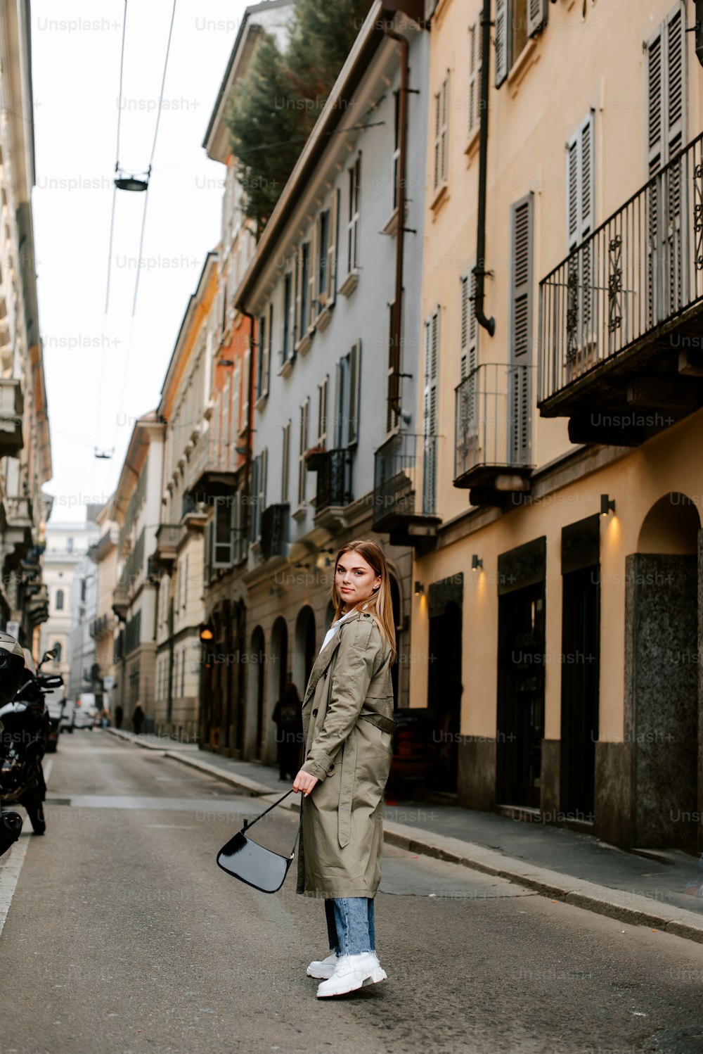 a woman in a trench coat is walking down the street