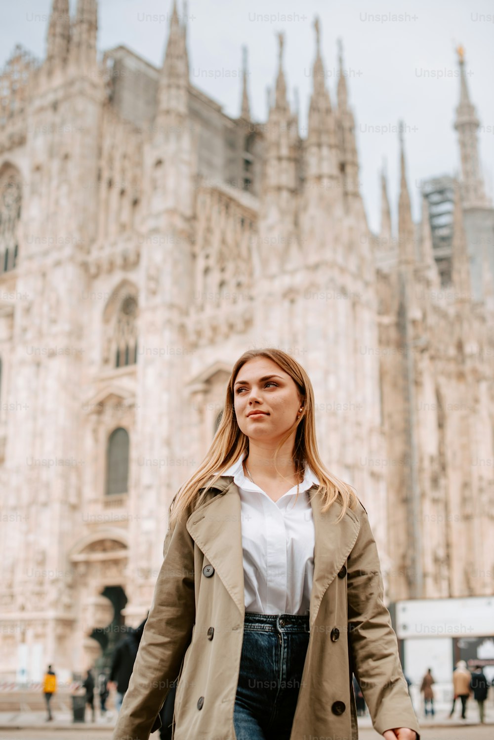 Una mujer con una gabardina está parada frente a una catedral