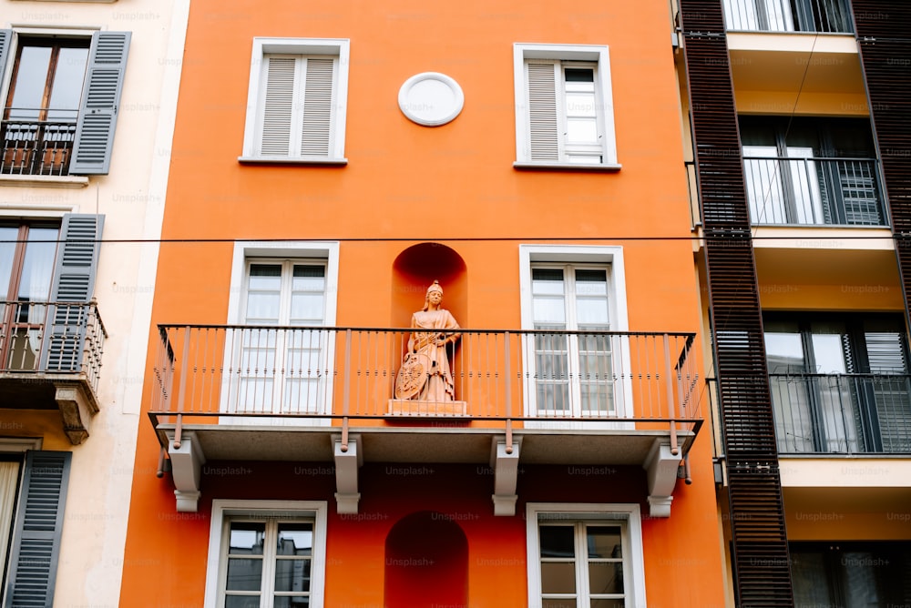 a tall orange building with a statue on the balcony
