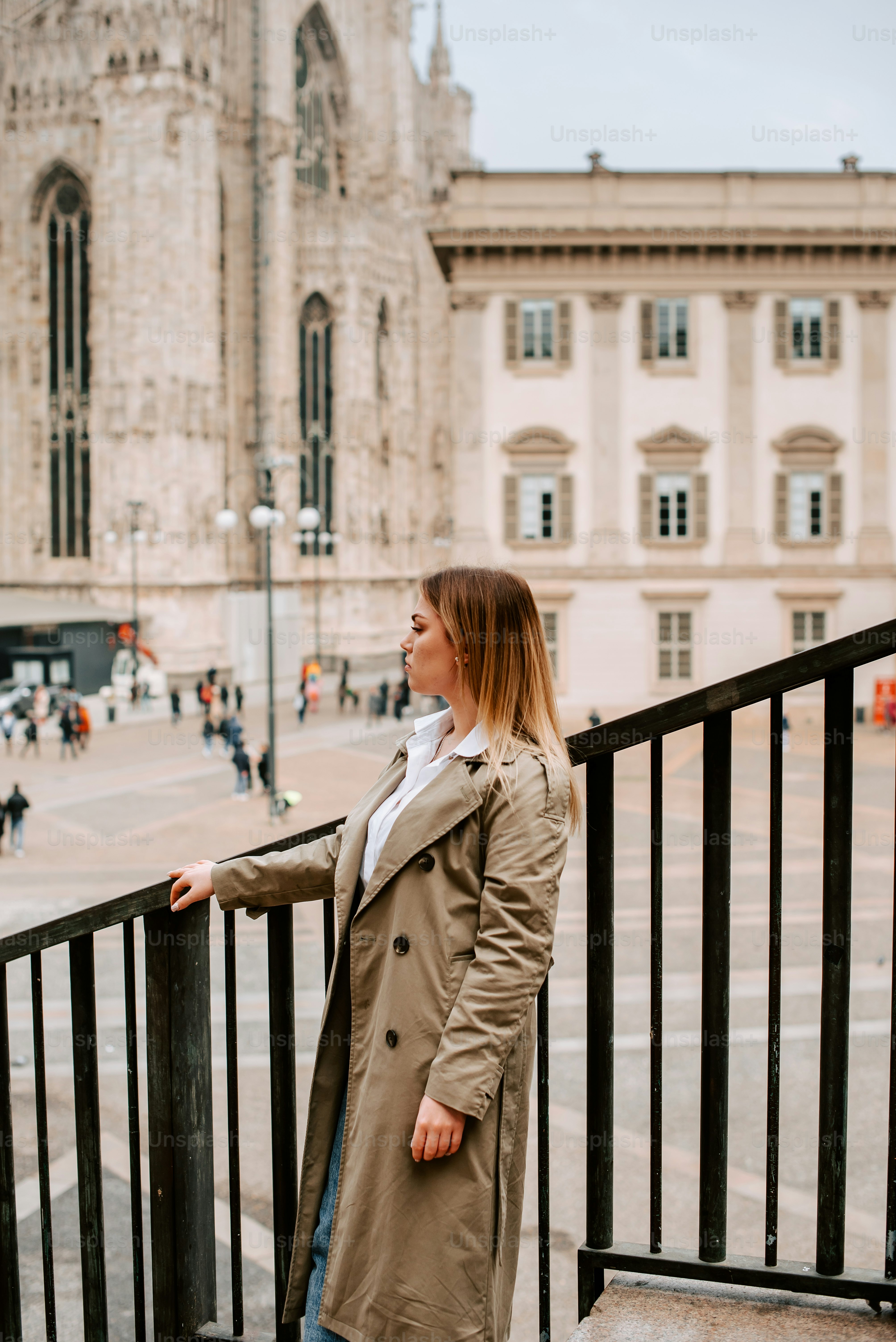 a woman in a trench coat standing on a balcony
