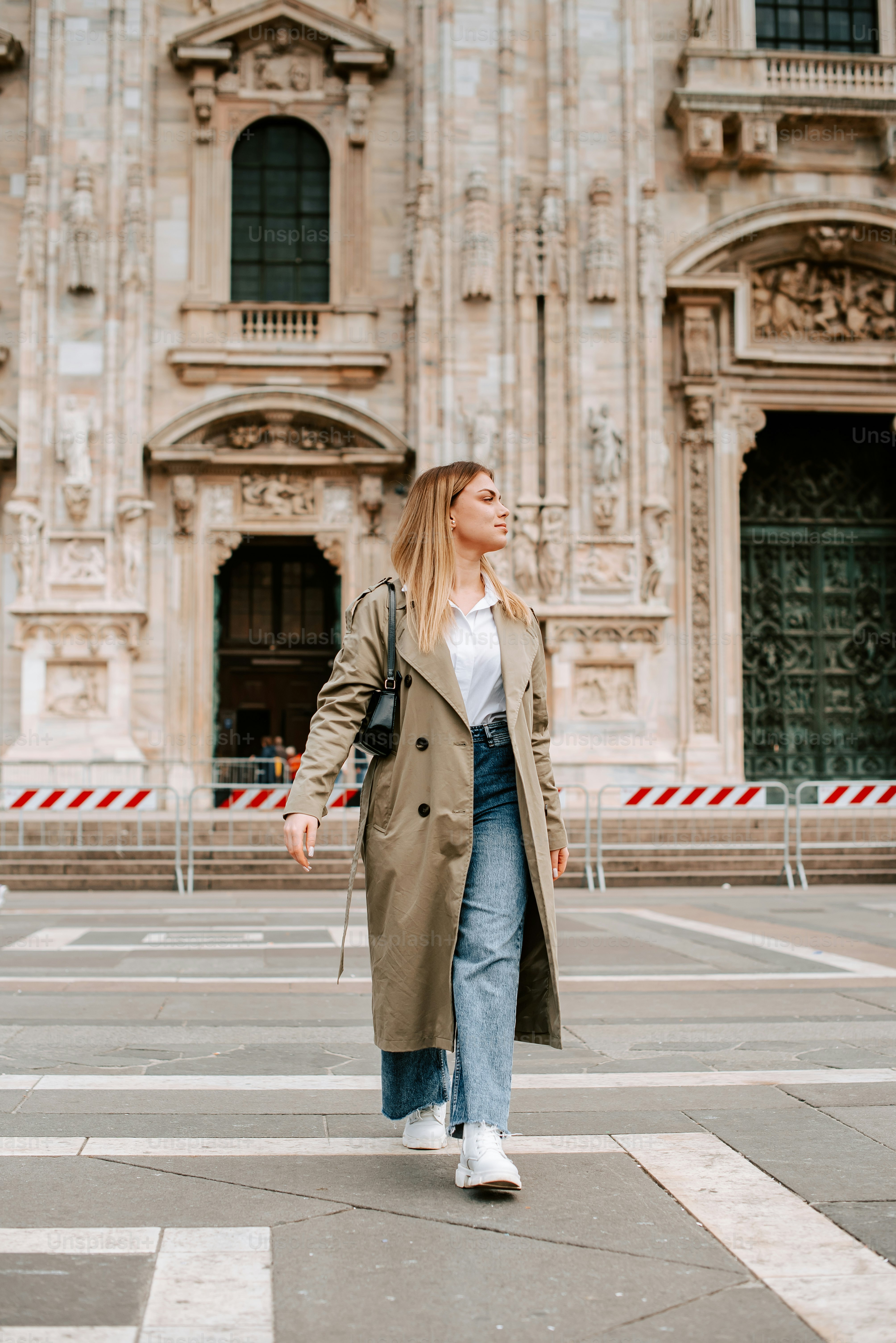 a woman in a trench coat is walking down the street