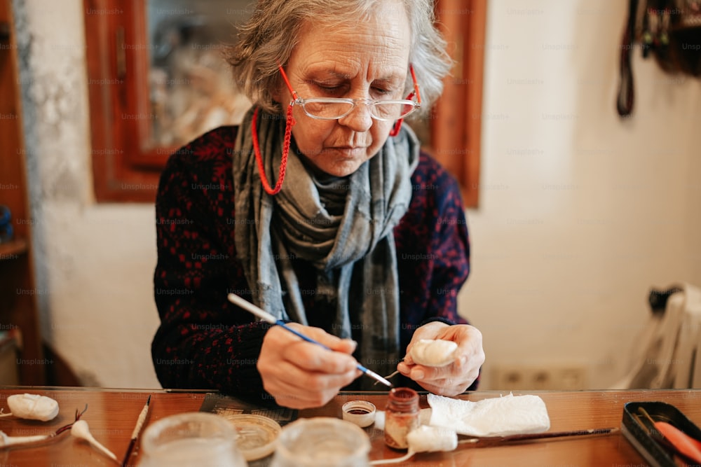 uma mulher mais velha está pintando um quadro em uma mesa