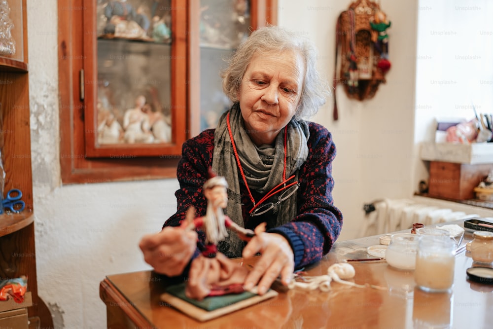 una donna anziana seduta a un tavolo con una bambola