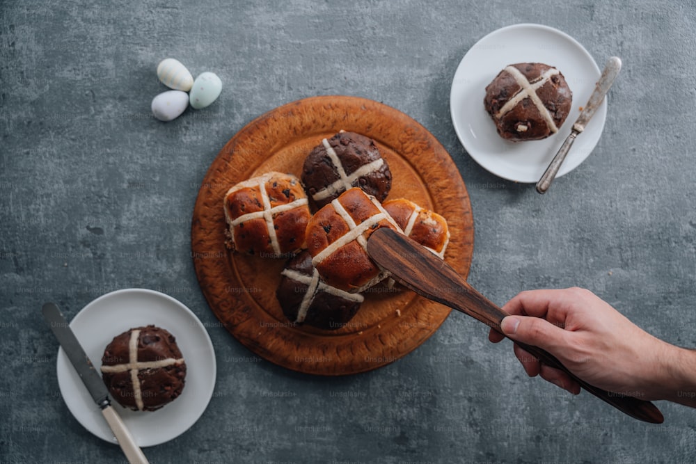 a person holding a wooden spoon over a plate of hot cross buns