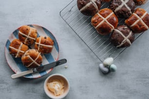 a plate of hot cross buns next to a plate of cupcakes