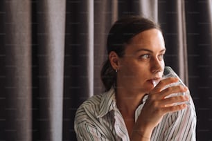 a woman drinking from a glass in front of a curtain
