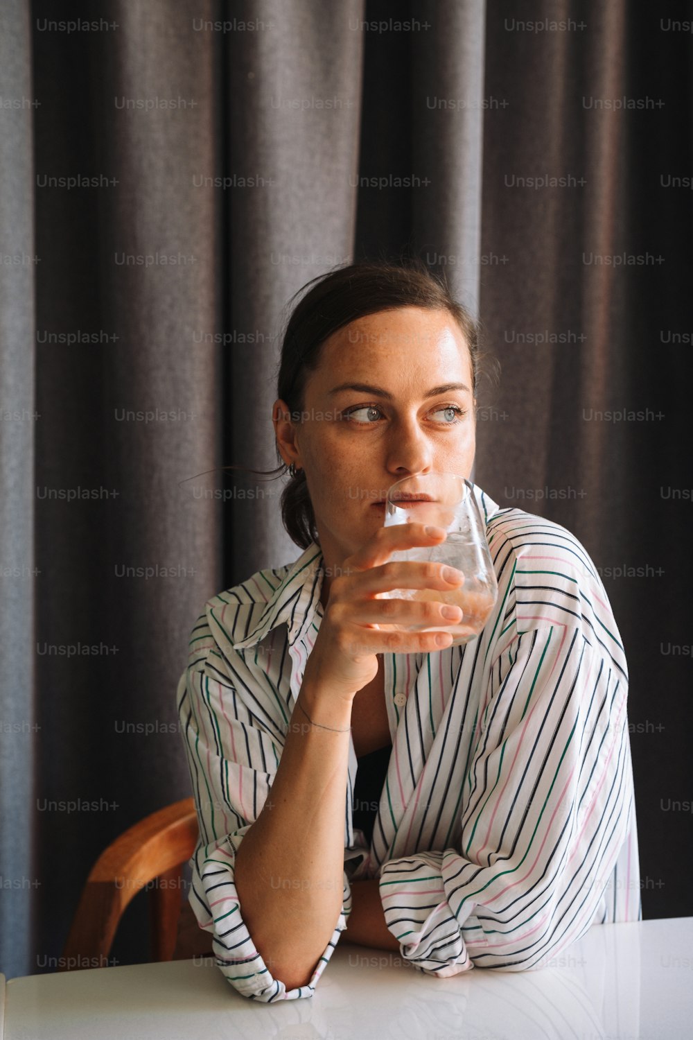 a woman sitting at a table drinking from a glass