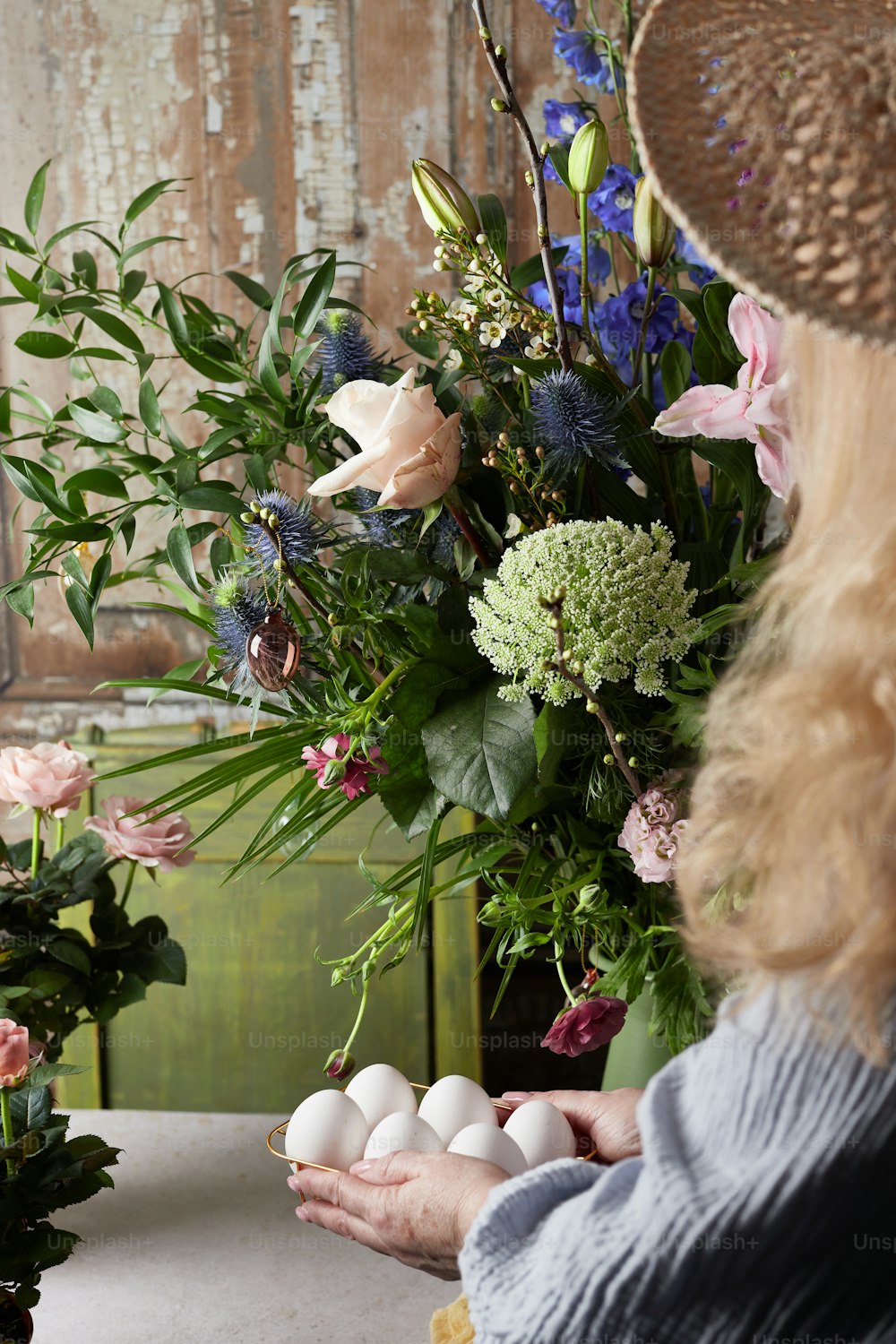 a woman in a straw hat holding eggs in front of flowers