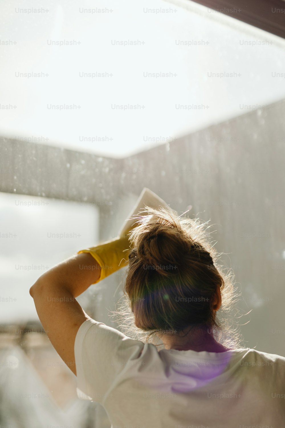 Eine Frau steht mit einem gelben Handschuh auf dem Kopf vor einem Fenster