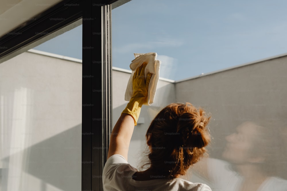 a woman cleaning a window with a yellow glove
