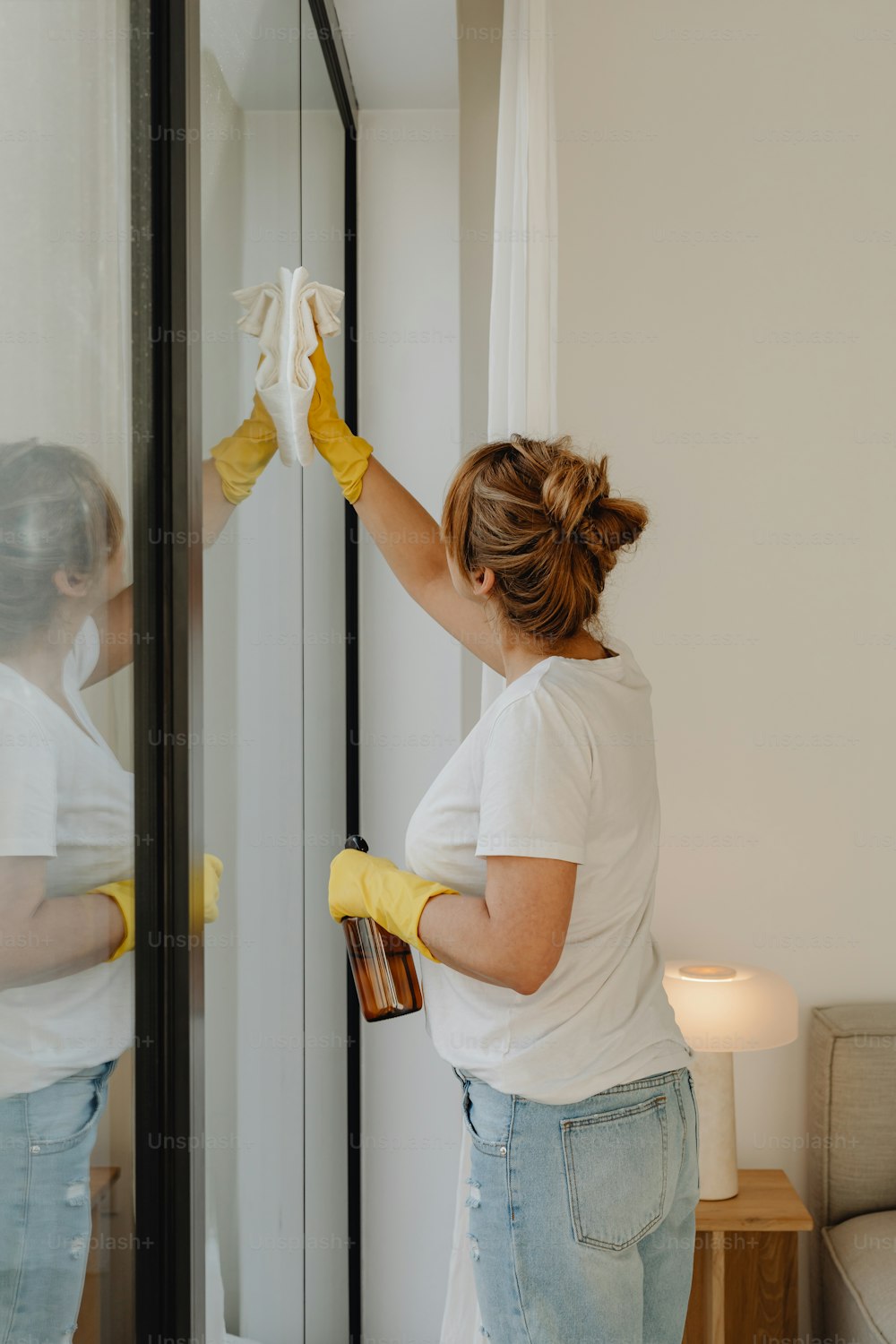 Une femme en chemise blanche et gants jaunes nettoyant un miroir