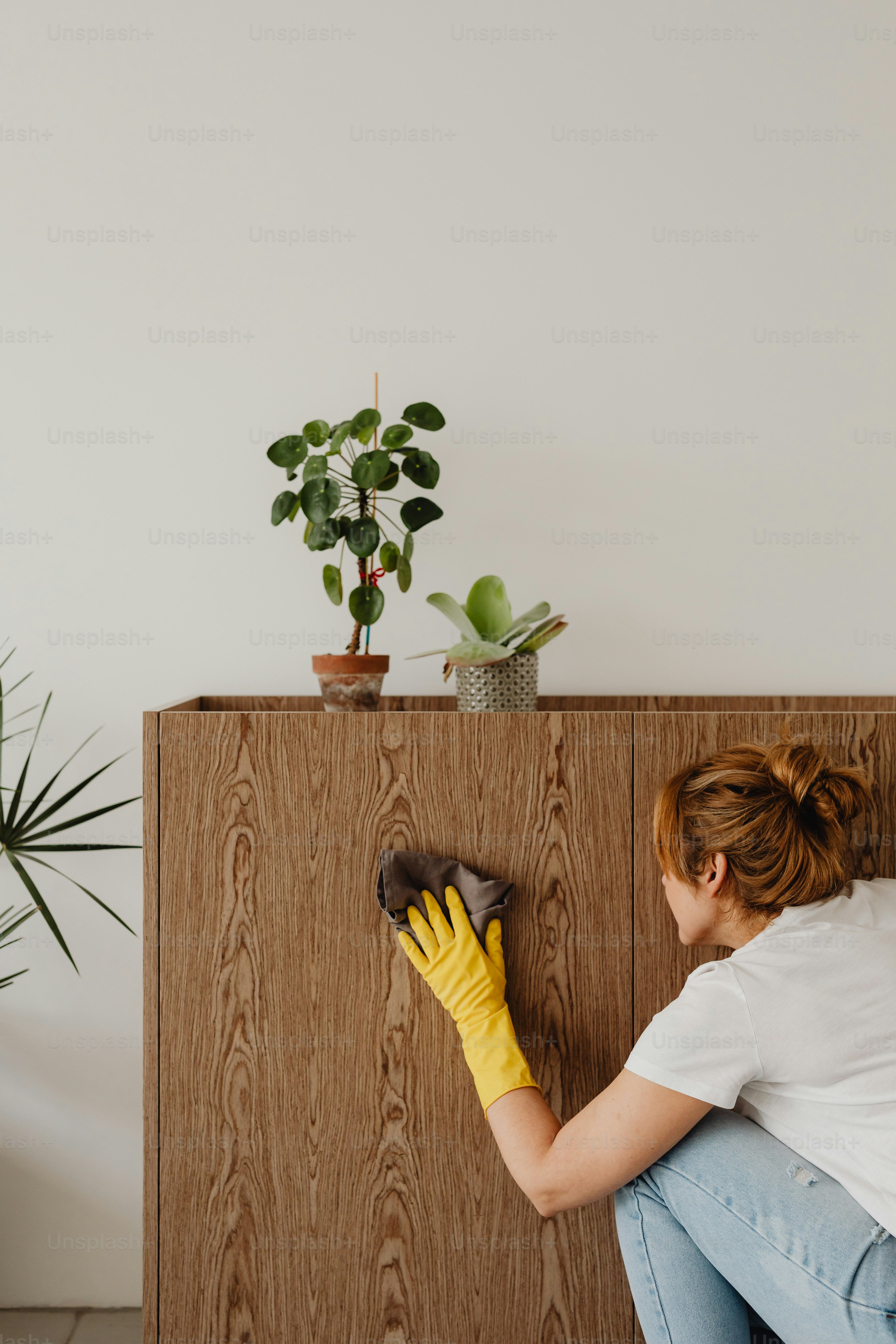 a woman in yellow gloves cleaning a wooden cabinet