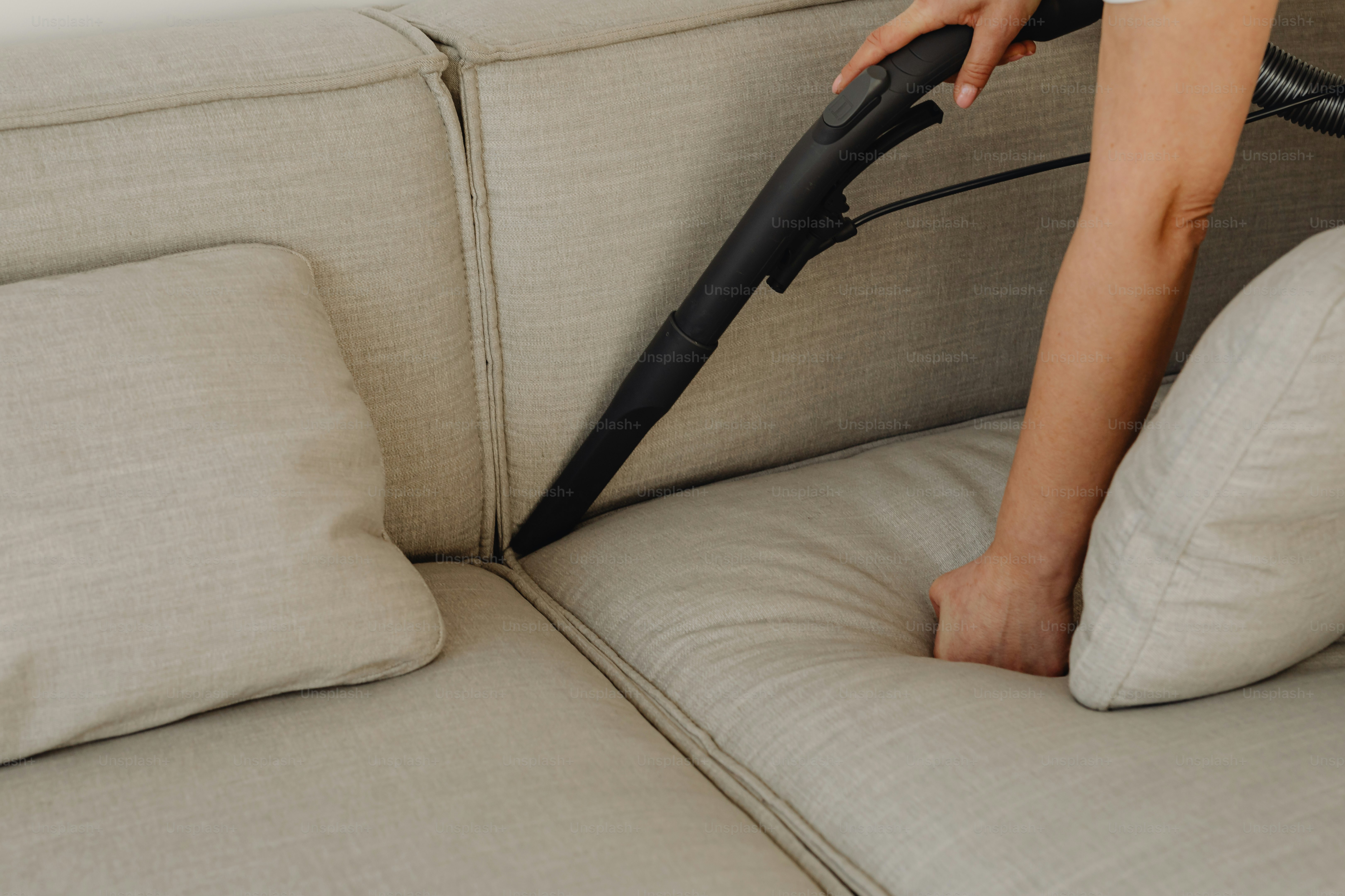 Eine Person, die einen Staubsauger benutzt, um eine Couch zu reinigen