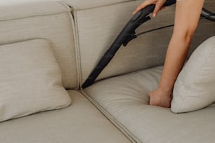 una persona que usa una aspiradora para limpiar un sofá