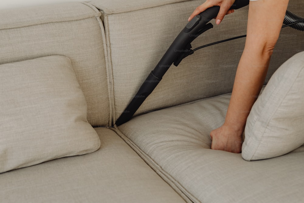 una persona che usa un aspirapolvere per pulire un divano