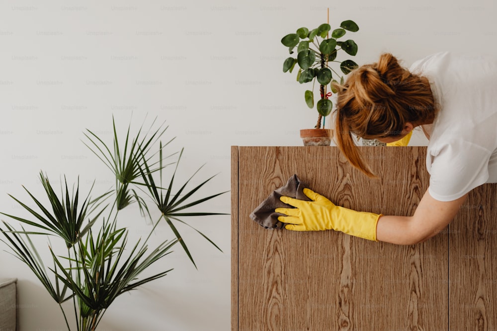a woman in a white shirt and yellow gloves cleaning a wooden cabinet
