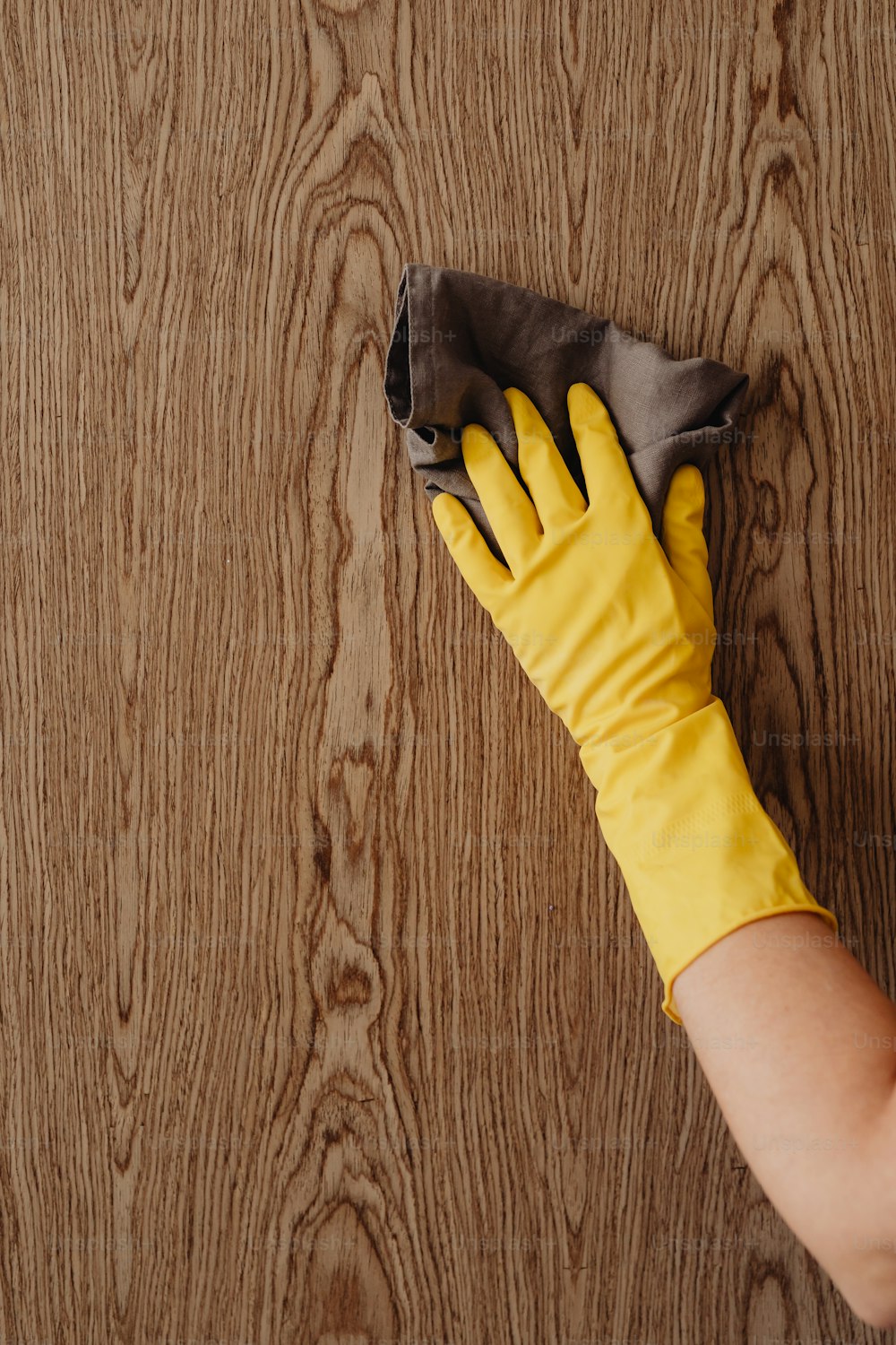 una persona che indossa guanti gialli che pulisce una superficie di legno