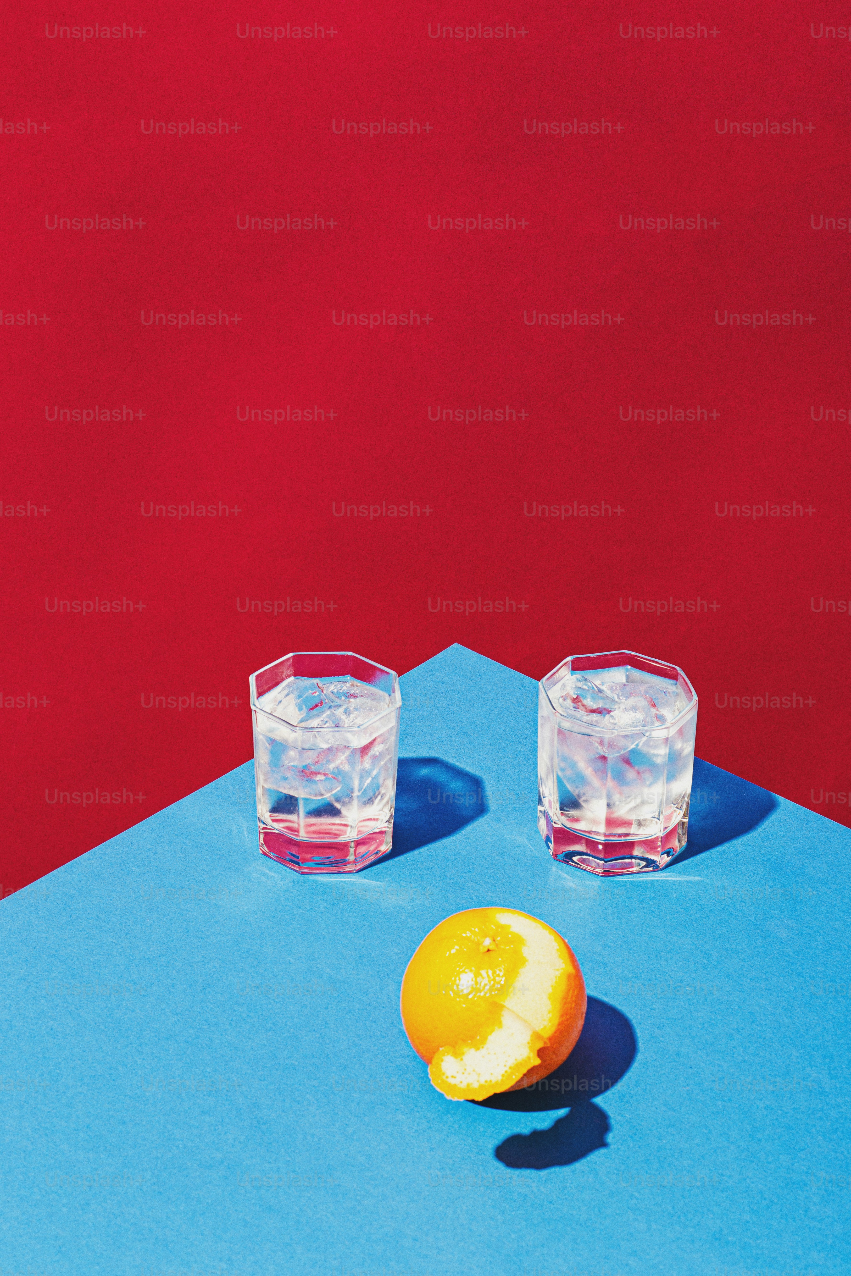 two glasses of water and an orange on a blue surface