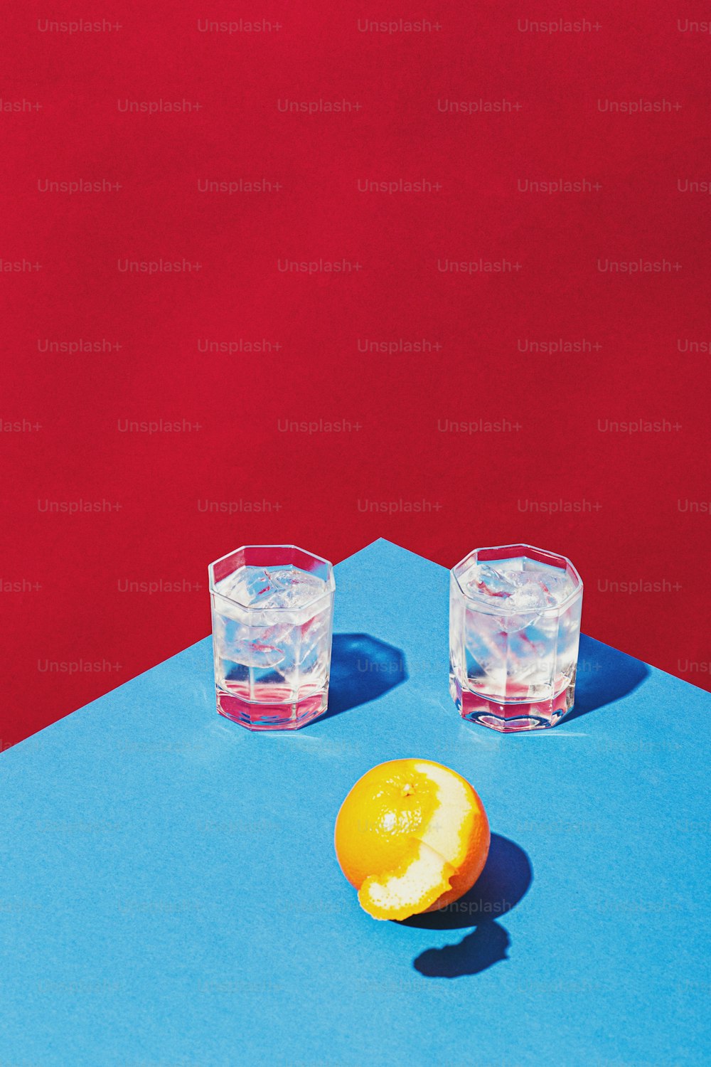 due bicchieri d'acqua e un'arancia su una superficie blu