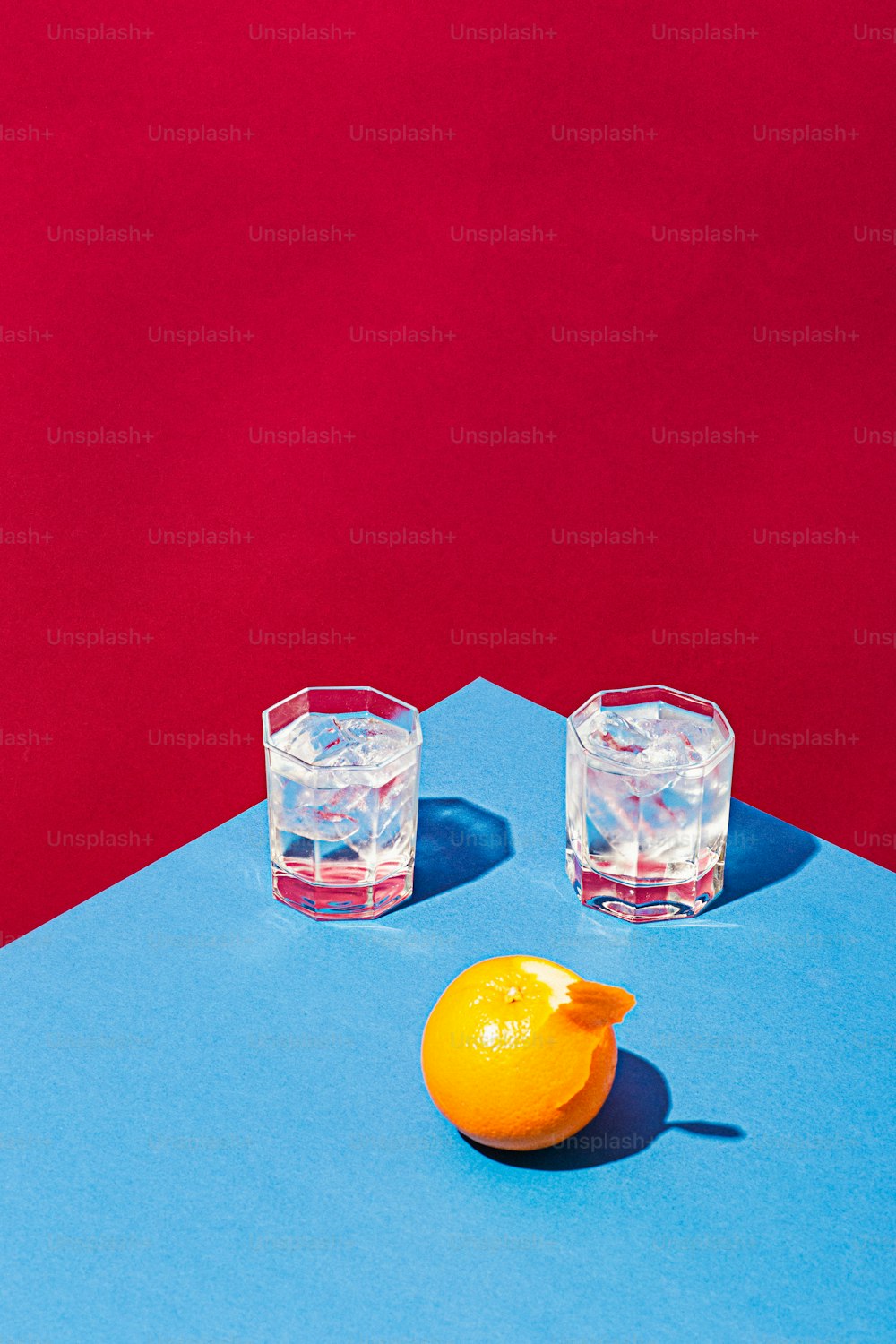 two glasses of water and an orange on a blue surface