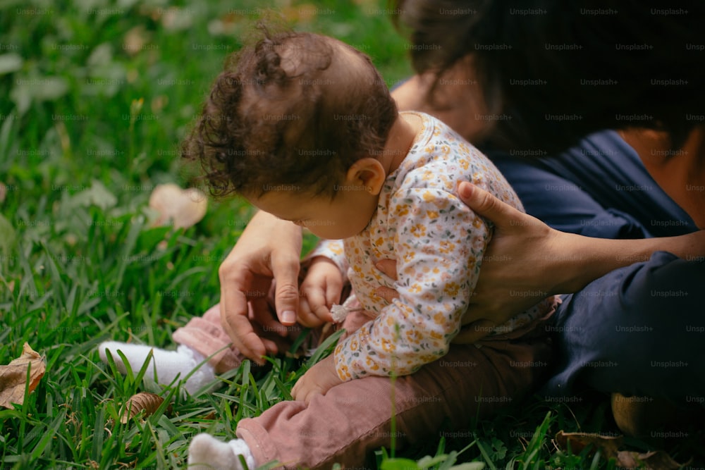 Eine Frau, die ein Baby auf dem Schoß im Gras hält