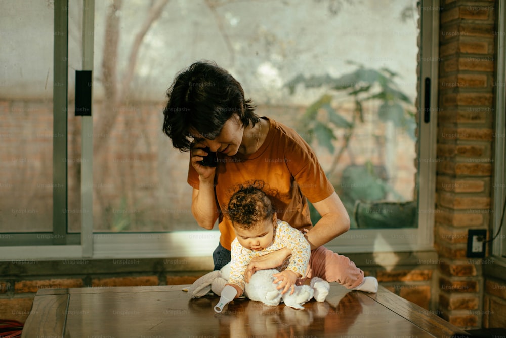 a woman holding a baby sitting on top of a wooden table