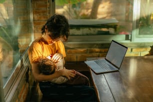 ノートパソコンの前で赤ん坊を抱えてテーブルに座っている男性