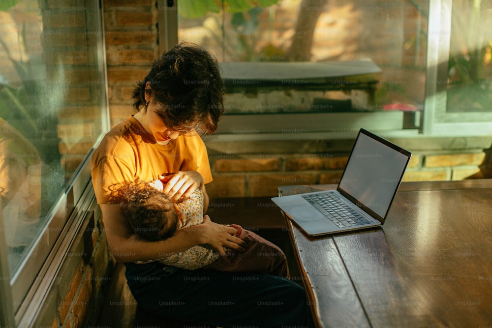 노트북 컴퓨터 앞에서 아기를 안고 테이블에 앉아 있는 남자