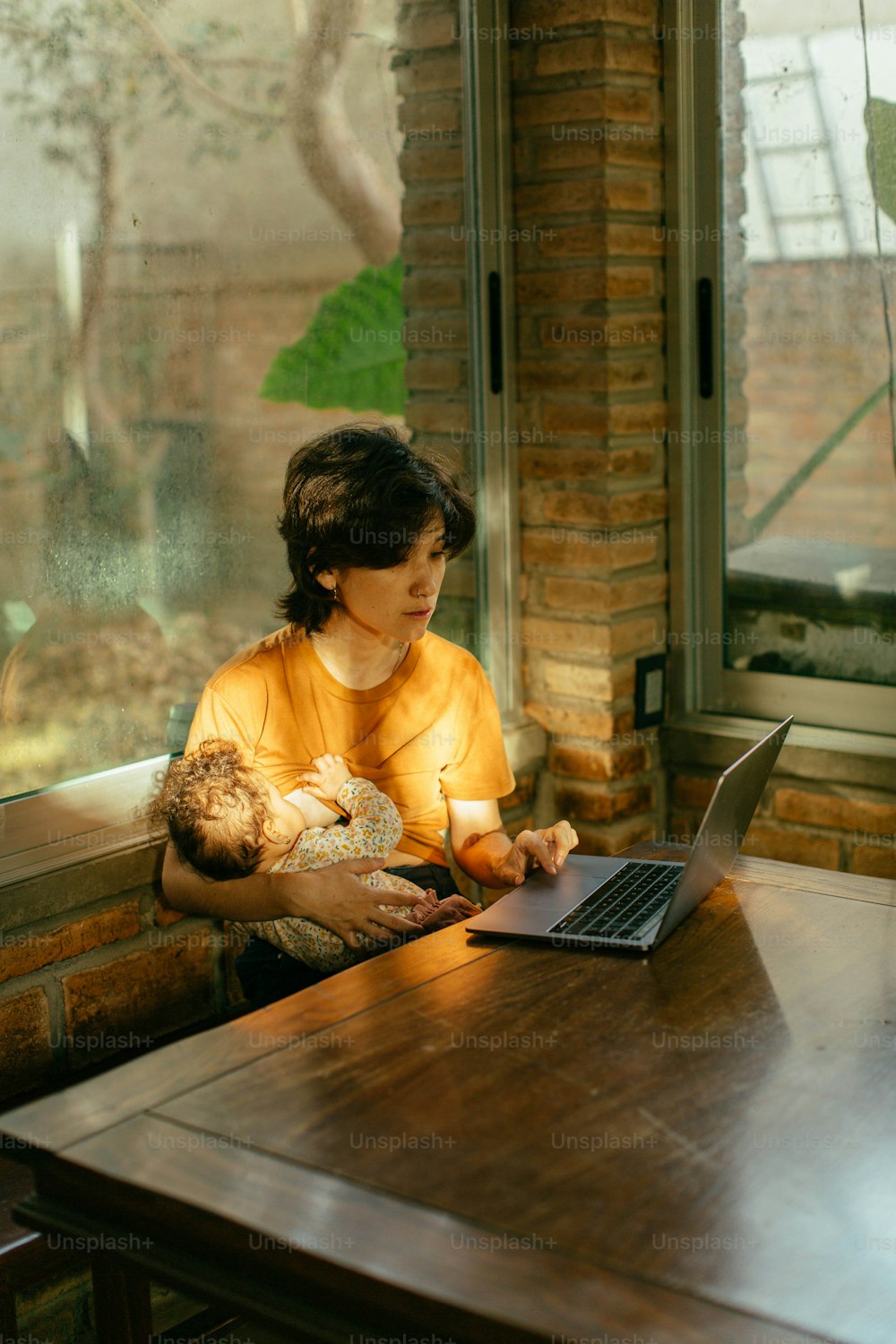 a woman sitting at a table with a baby and a laptop