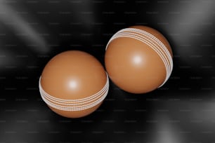two brown leather cricket balls on a black background