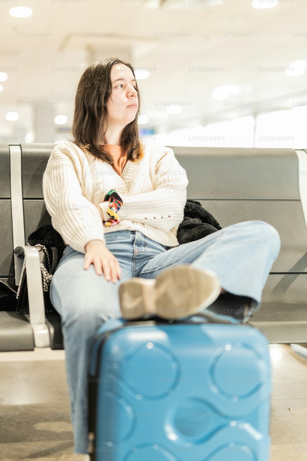 a woman sitting on a bench next to a blue suitcase