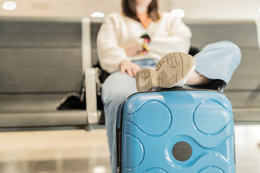 Una mujer sentada en un banco junto a una maleta azul