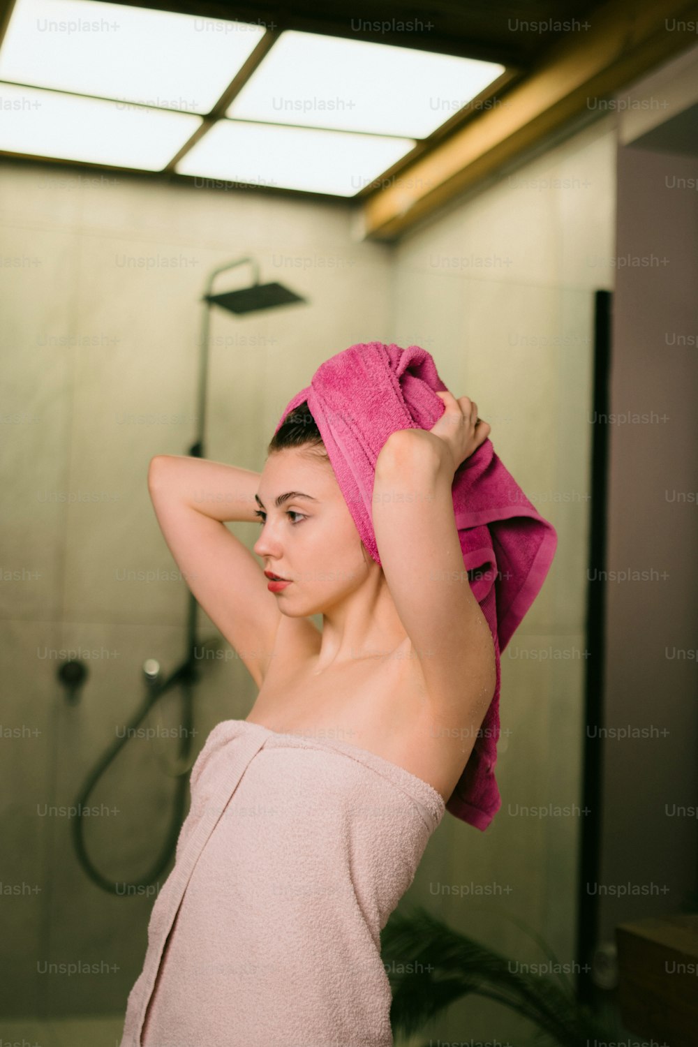 수건을 쓴 여자가 샤워 앞에 서 있다