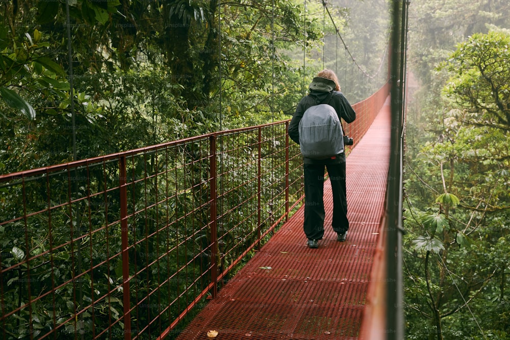 a man walking across a suspension bridge in the jungle