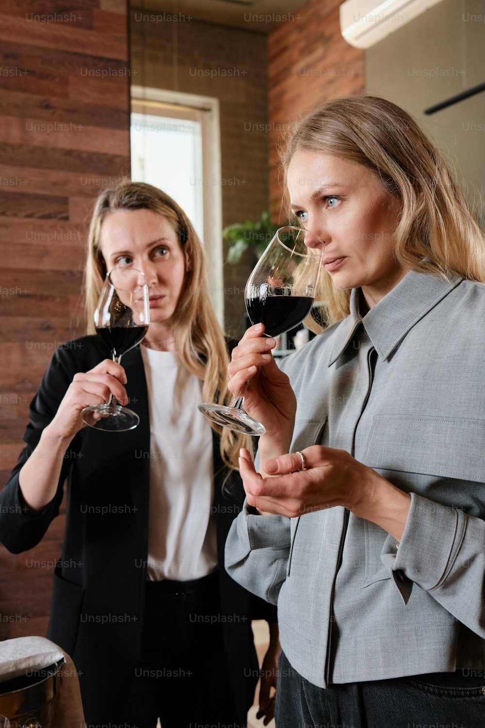 duas mulheres em pé uma ao lado da outra segurando taças de vinho