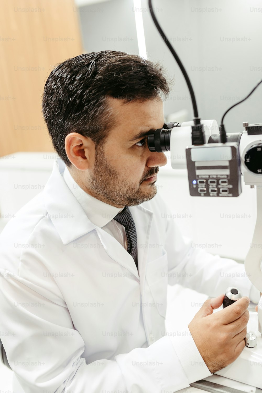 a man in a white shirt and tie looking through a microscope