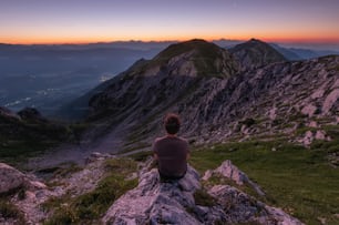 Una persona sentada en una roca mirando las montañas