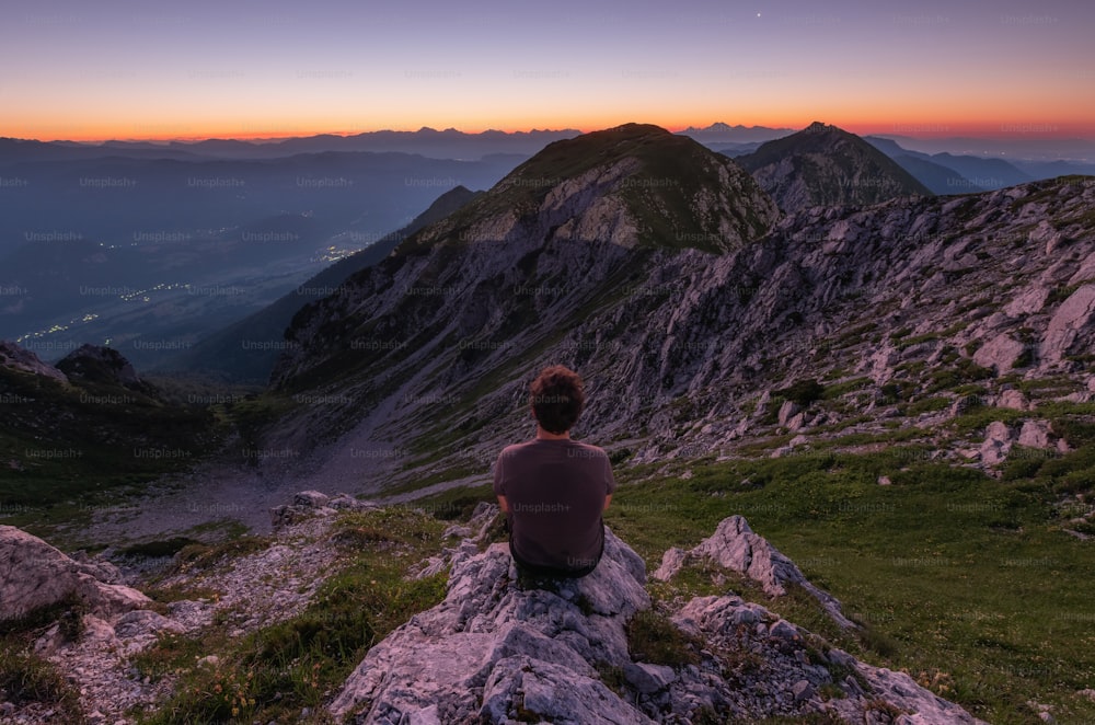 una persona seduta su una roccia che guarda le montagne