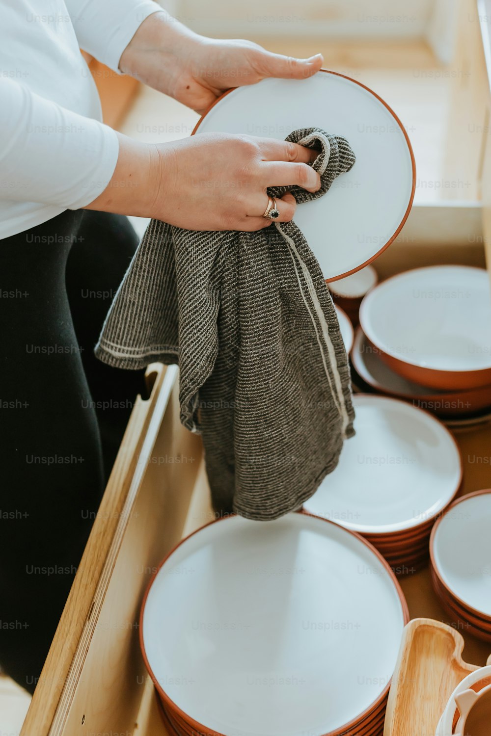 a person holding a cloth over a drawer full of dishes