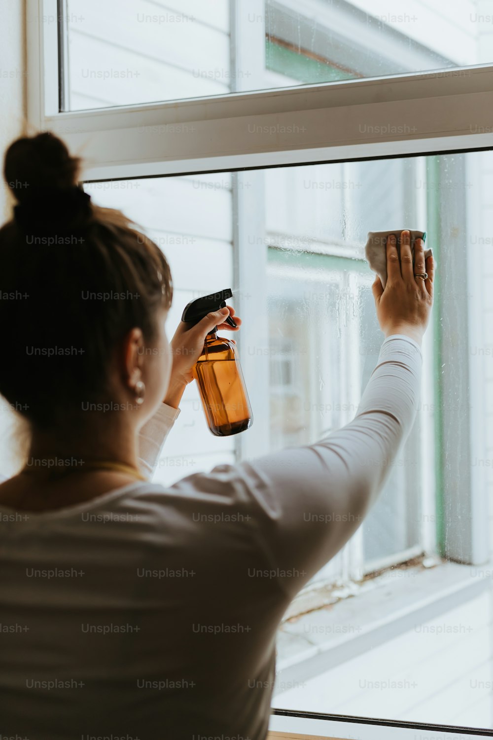 a woman is cleaning a window with a sprayer