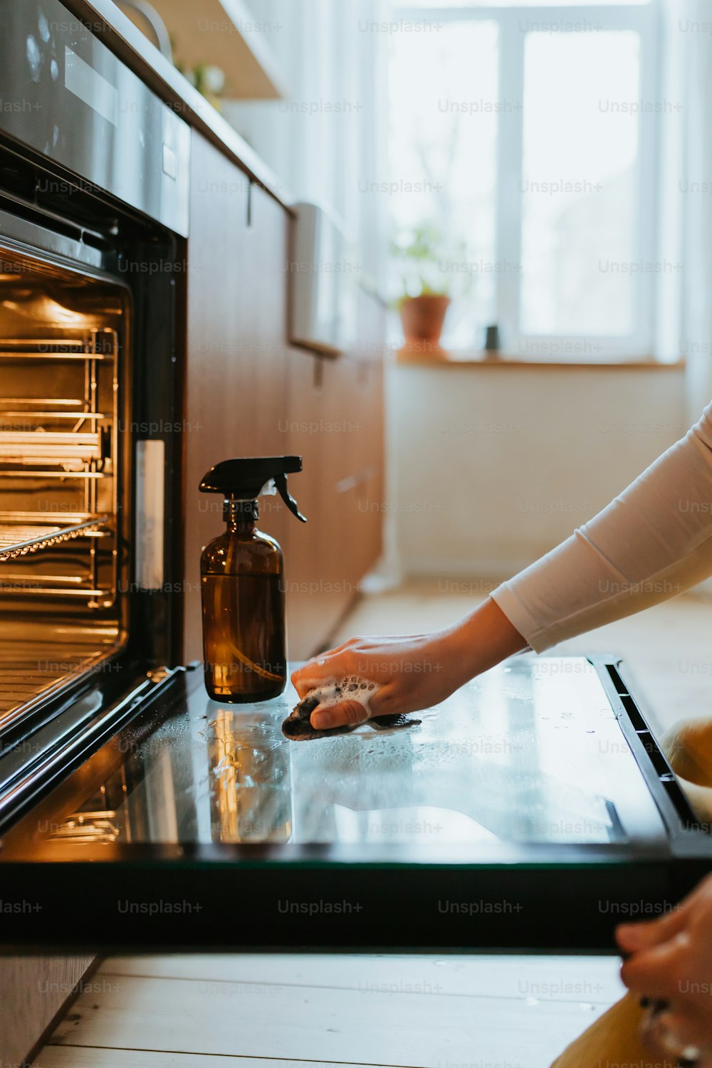 Una mujer está limpiando el horno con una botella de spray