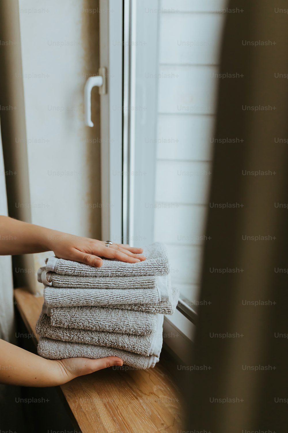 a person holding a stack of towels in front of a window